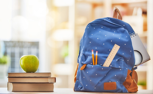 Apfel, Stapel von Büchern und Rucksack auf dem Schreibtisch.