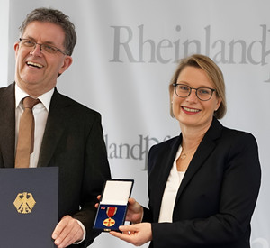Das Foto zeigt Bildungsministerin Dr. Stefanie Hubig und Ulf Störmer. Er hält seine Urkunde, die Ministerin die Verdienstmedaille in die Kamera. 