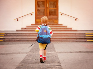 Ein kleines Kind mit Rucksack läuft einem Gebäude zu