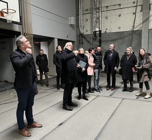 Das Foto zeigt Ministerin Hubig im Gespräch mit Schulleiter Dr.Braner während eines Rundgangs durch die Sporthalle des Rhein-Gymnasiums. Im Hintergrund sind weitere Beteiligte zu sehen. 