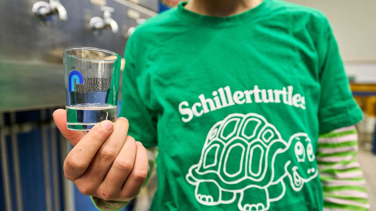 Zu sehen ist ein Kinder der Schillerschule Lahnstein, welches ein Glas mit Trinkwasser in die Kamera hält. 