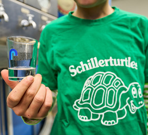 Zu sehen ist ein Kinder der Schillerschule Lahnstein, welches ein Glas mit Trinkwasser in die Kamera hält. 