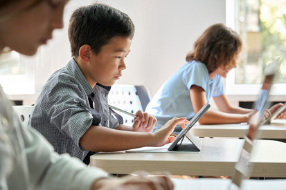 Fokussierter asiatischer Schüler mit digitalem Tablet im Unterricht. 
