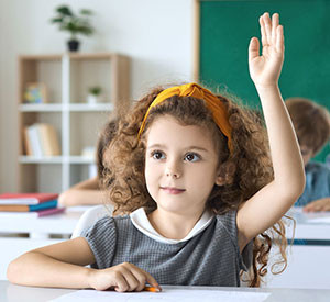 Eine Schülerin der Grundschule hebt ihre Hand und ist bereit, die Fragen der Lehrerin im Unterricht zu beantworten.