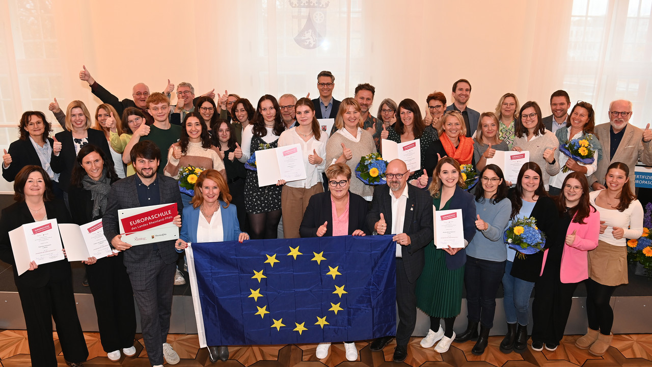 Gruppenbild der ausgezeichneten Europaschulen. Vorne im Bild halten Staatsekretärin Brück und Staatsekretärin Raab eine Europafahne. 