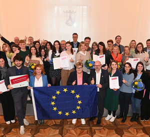 Gruppenbild der ausgezeichneten Europaschulen. Vorne im Bild halten Staatsekretärin Brück und Staatsekretärin Raab eine Europafahne. 