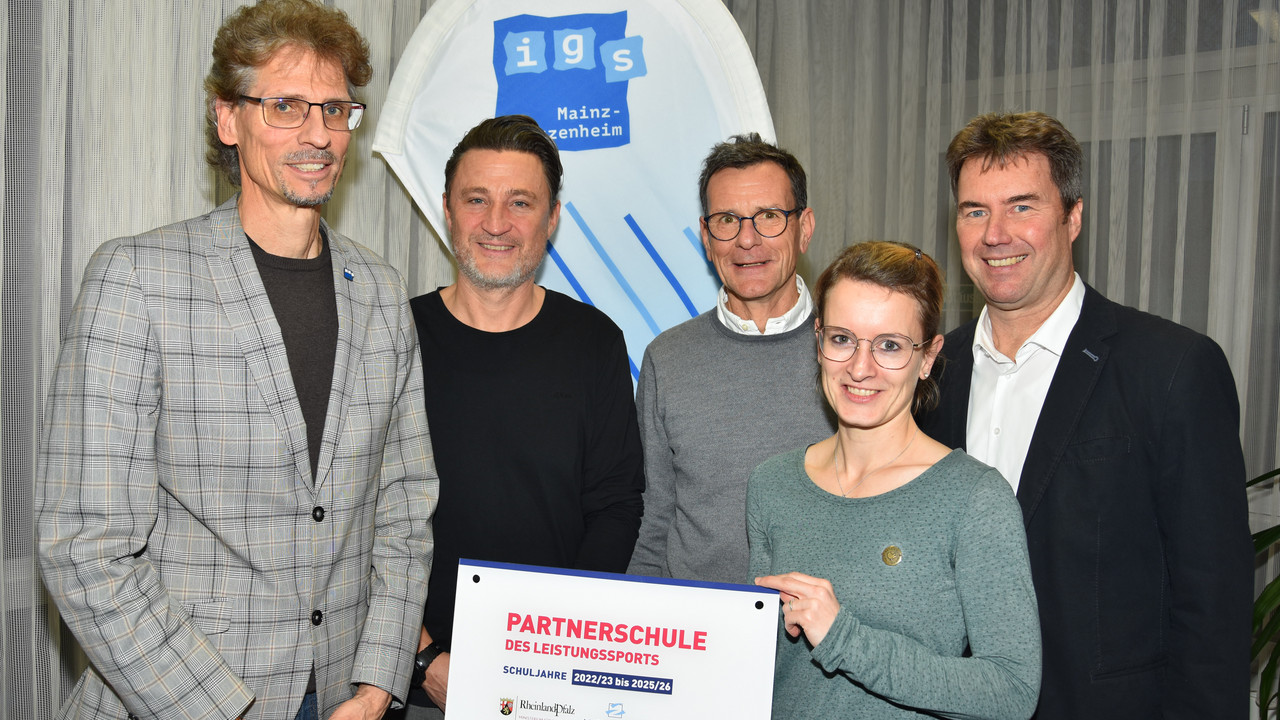 Das Foto bildet die offizielle Übergabe des begehrten Schildes ab. Von links nach rechts sind auf dem Foto zu sehen: Roland Wollowski (Schulleiter IGS Bretzenheim), Stefan Klören (Sportzweigleiter IGS Bretzenheim), Michael Stäudt (Mitarbeiter Schulsportreferat im Ministerium für Bildung RLP), Melanie Heß (LSB-Referentin für Leistungssport), Volker Weiß (Schulsportreferent im Ministerium für Bildung RLP)