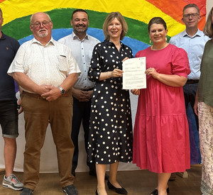 Staatssekretärin Jenny Groß (Mitte) übergibt den Förderbescheid an die Pfarrer-Giesendorf-Grundschule in Dernbach.