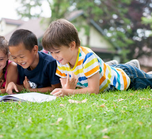 Drei Kinder liegen auf einer Wiese und lesen dabei gemeinsam ein Buch.