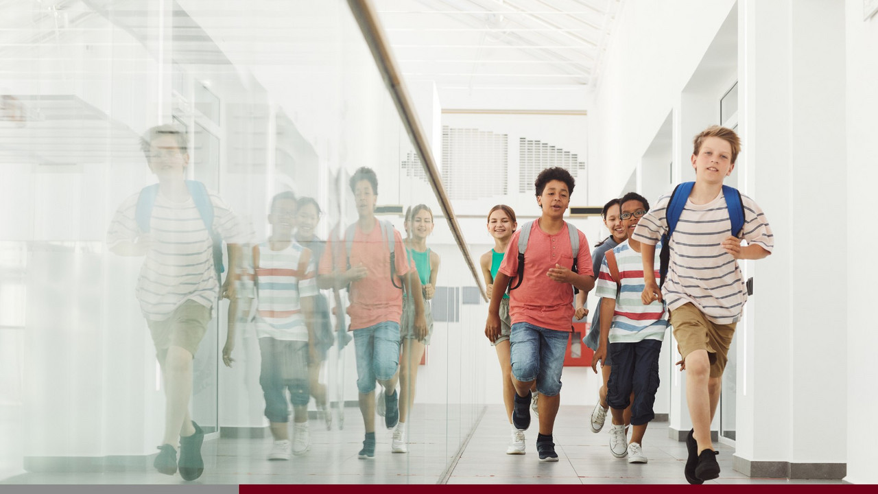 Symbolbild: Schülerinnen und Schüler die in einem offen und hell gestalteten Foyer laufen. 